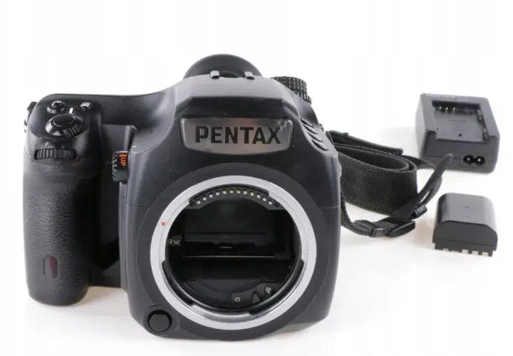 Czarna lustrzanka cyfrowa Pentax z paskiem i akcesoriami, gotowa do aukcji na Allegro.