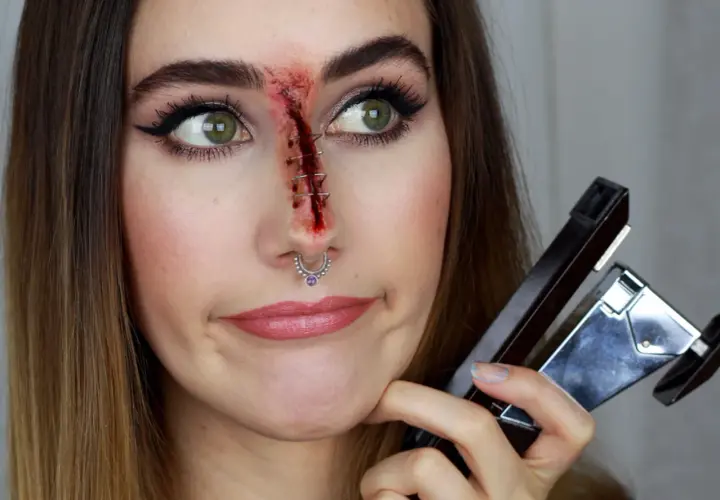 Sista minuten halloween sminkning: ett sår med häftklamrar på näsan, en häftapparat i handen.