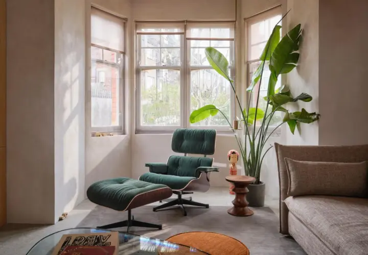 Ein gemütliches Mid-Century-Wohnzimmer mit einem grünen Sessel und Hocker, einer großen Zimmerpflanze und einem beigen Sofa.