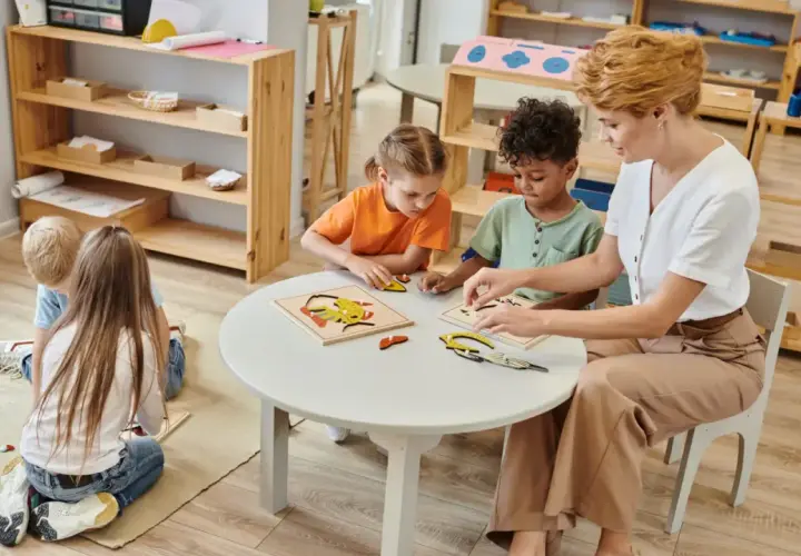 Niños y maestra armando rompecabezas en una mesa. Es normal que los niños se toquen entre ellos mientras aprenden y juegan juntos.