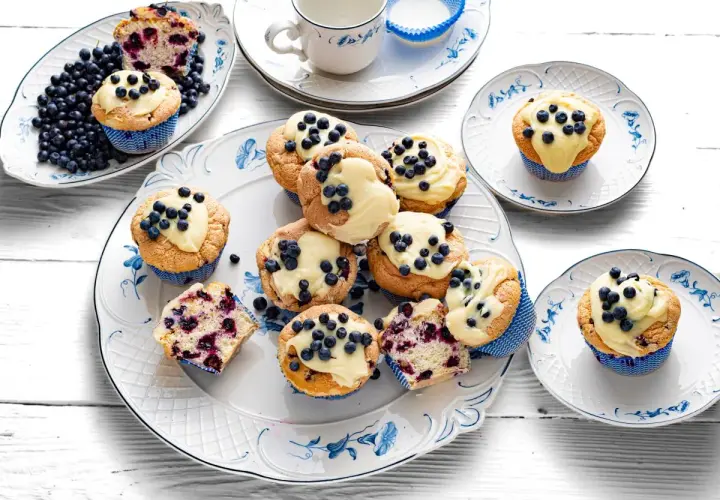 Pyszne muffiny z jagodami, udekorowane kremem i świeżymi owocami, kuszą swoim wyglądem i zapachem.