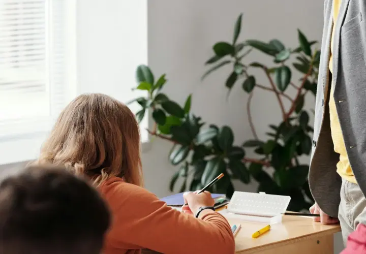 Ein Mädchen konzentriert sich auf seine Aufgaben während der Freiarbeit in der Grundschule. Ein Lehrer steht daneben.