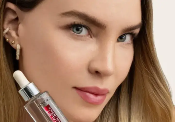 Mujer con cabello rubio y joyas brillantes sostiene un frasco de sérum, parte de su rutina de cuidado de la piel.