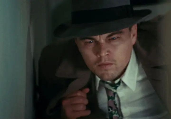 Leonardo DiCaprio, dans la distribution de Shutter Island, porte un chapeau et un trench-coat, l'air intense et méfiant.