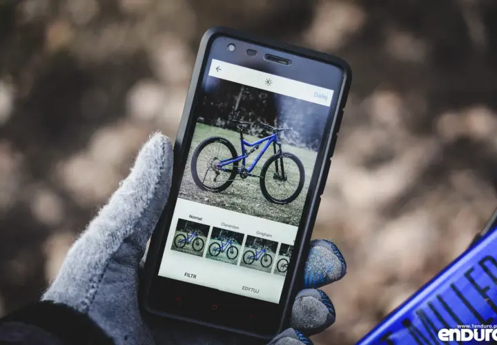 Rękawiczka trzyma smartfon z niebieskim rowerem na ekranie. Aplikacja oferuje filtry, jak w mapach rowerowych.
