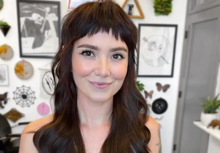 Uśmiechnięta kobieta z ciemnymi włosami i odważnymi baby bangs.