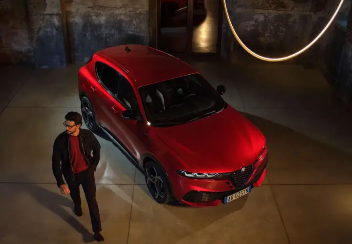 Elegancki mężczyzna w okularach obok lśniącego, czerwonego Alfa Romeo Tonale. Sprawdź aktualną alfa romeo tonale cena i odkryj jego styl.