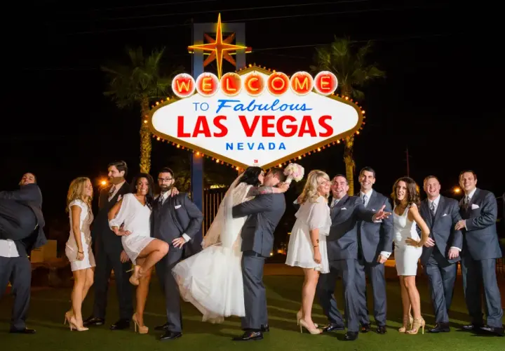 Ślub w Las Vegas jest ważny w Polsce? Para młoda całuje się pod neonem "Welcome to Fabulous Las Vegas", otoczona przez świadków.