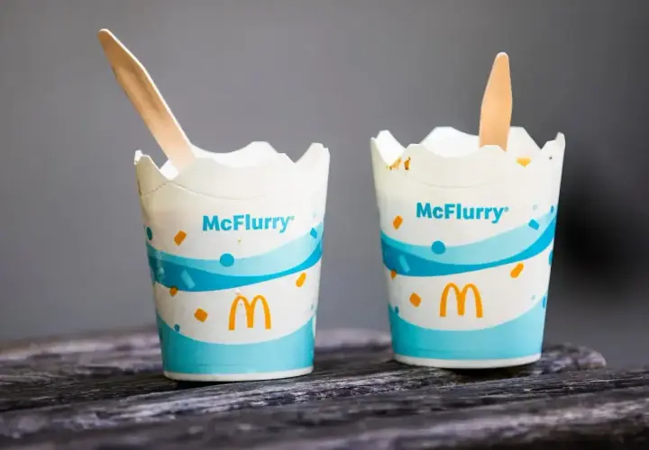 Dwa kubki McFlurry McDonald's z drewnianymi łyżeczkami na drewnianym blacie.