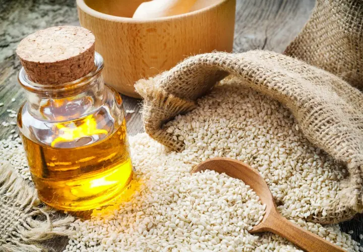 Olio di sesamo dorato in bottiglia, semi di sesamo in un sacco di juta e un cucchiaio di legno. Scopri le incredibili olio di sesamo proprietà.