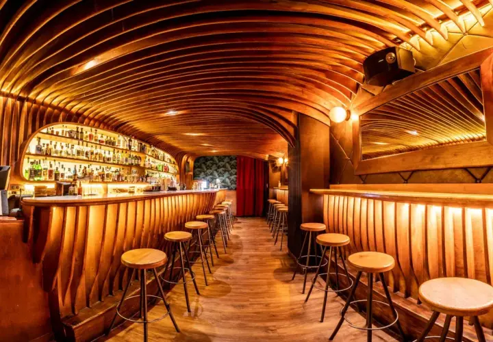 Bar de madera con estantes llenos de botellas, taburetes y un techo curvo. ¡Cosas curiosas que ver en Barcelona!