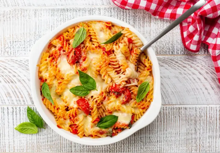 Un plat de pâtes fusilli gratinées avec une sauce tomate savoureuse et du fromage fondant, garni de feuilles de basilic frais.