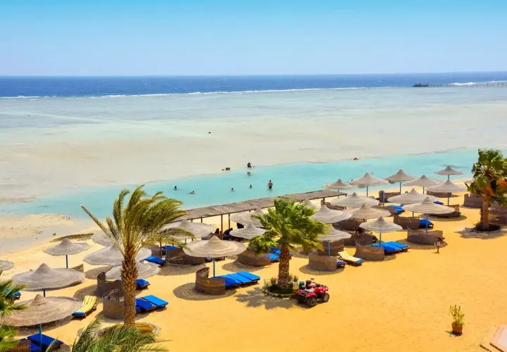 Piękna plaża z palmami i leżakami, idealna na wakacje. Wiele osób pływa w turkusowej wodzie. Blue Reef Resort opinie potwierdzają rajski wypoczynek.