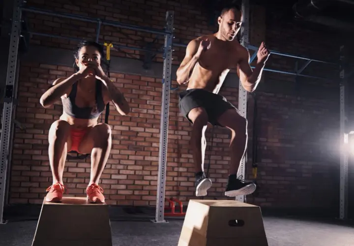 Para i mężczyzna wykonują trening crossfit, skacząc na skrzynie.