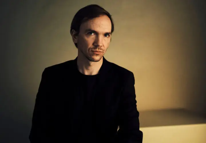 Portret Jana Komasy, reżysera znanych filmów. Jego spojrzenie sugeruje głębię i skupienie, jak w jego kinowych dziełach.