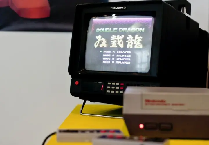 Stary telewizor Thomson z grą Double Dragon. Na ekranie widoczna lista trybów gry, np. "MODE A 1PLAYER". Obok konsola Pegasus.