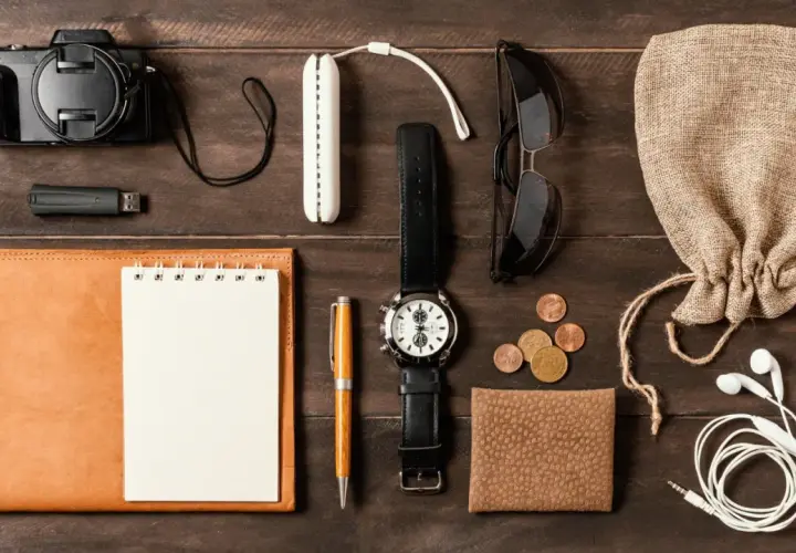 Zestaw EDC: aparat, pendrive, notes, długopis, zegarek, okulary, monety, portfel, słuchawki i woreczek.