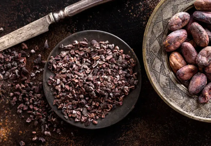 Un coltello d'argento accanto a una ciotola di **semi di cacao** tritati e un piatto decorato con semi di cacao interi.