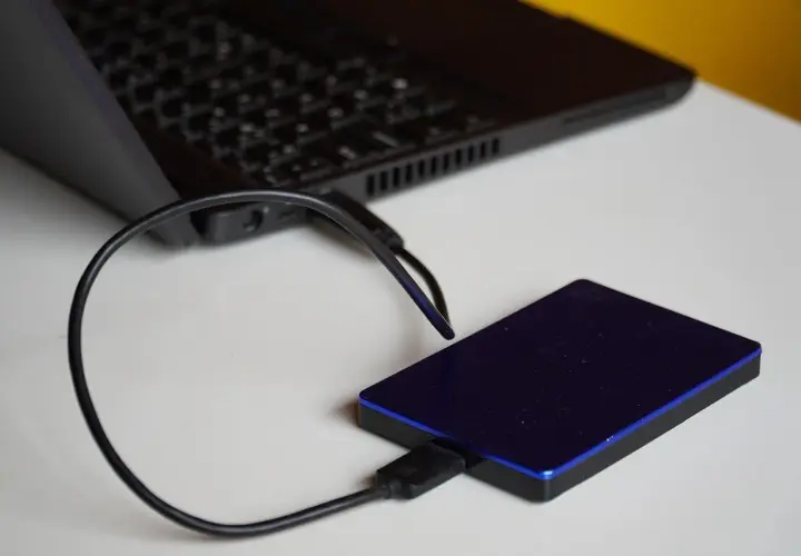 Un disque dur externe bleu est connecté à un ordinateur portable. Un guide pour comment choisir son disque dur externe.