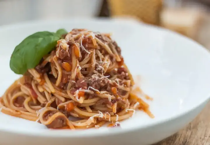 Pyszne spaghetti z sosem ragu, posypane parmezanem i udekorowane listkiem bazylii. Idealny przepis na obiad.