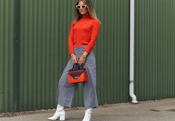Spodnie kuloty dla jakiej sylwetki? Modelka w kraciastych spodniach kulotach i pomarańczowym golfie prezentuje stylową propozycję.