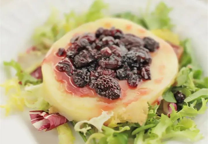 Provolone a la plancha cubierto con moras y salsa, servido sobre una cama de lechugas mixtas.