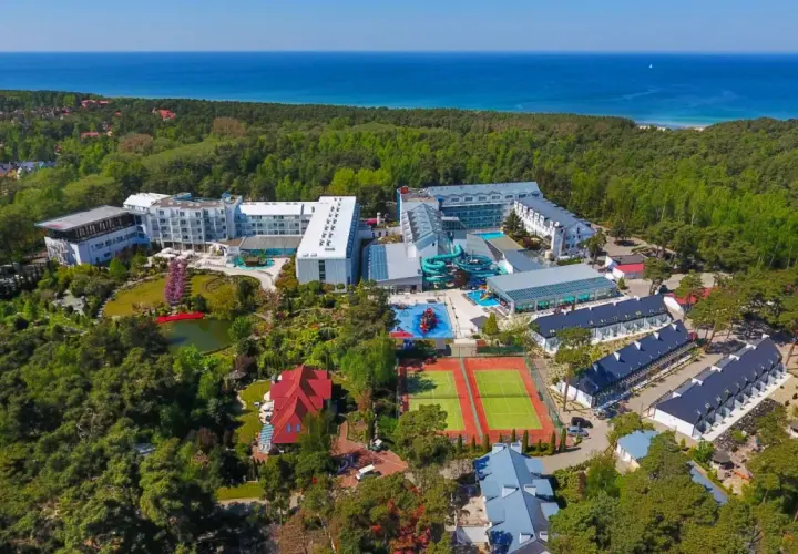 Widok z lotu ptaka na aquapark Pobierowo otoczony lasem, z widokiem na morze. Kompleks oferuje baseny, zjeżdżalnie i korty tenisowe.