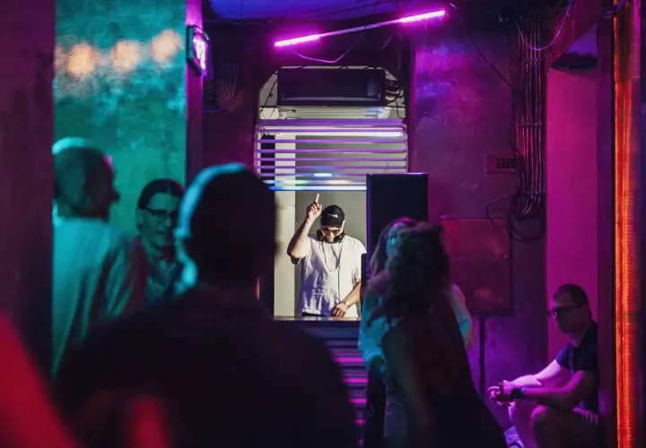 DJ w klubie, podniesiony palec, neonowe światła, różowy sober tekst.