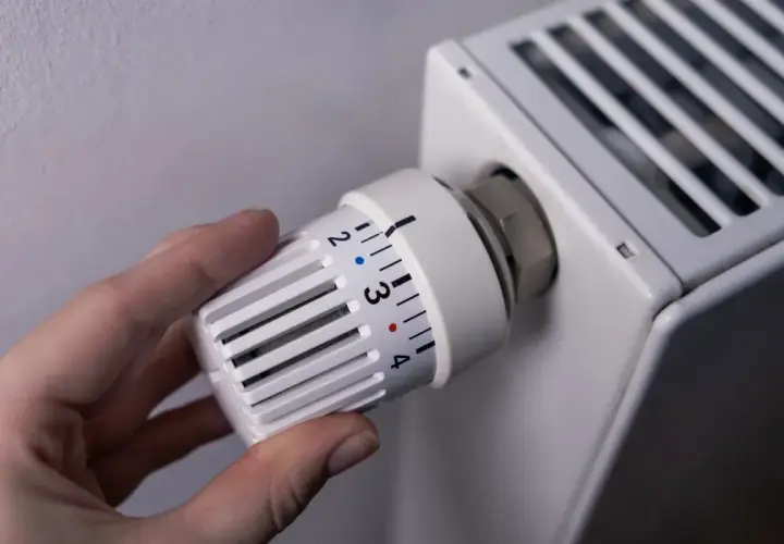 Dłoń reguluje termostat grzejnika, kontrolując ogrzewanie domu na gaz. Ustawienie temperatury na 3.