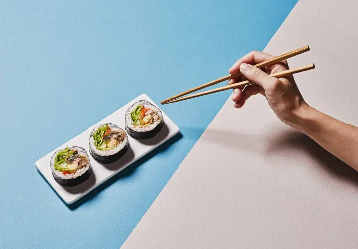 Dłoń z pałeczkami do sushi pokazuje, jak trzymać pałeczki do sushi, by złapać pyszne rolki.