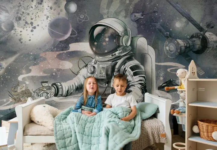 Dzieci siedzą pod kołdrą na łóżku, a za nimi wspaniała tapeta kosmos dla dzieci z astronautą i planetami.