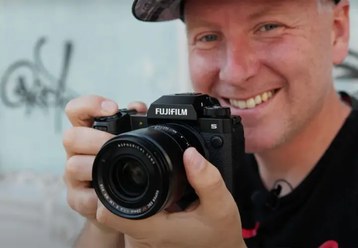 Uśmiechnięty mężczyzna trzyma aparat Fujifilm XH2S z obiektywem.