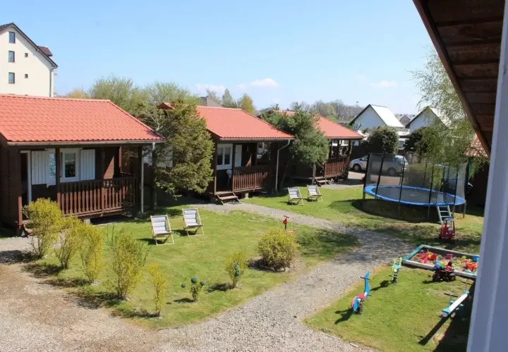 Ustronie Morskie centrum: drewniane domki z czerwonymi dachami, plac zabaw z trampoliną i piaskownicą, leżaki na trawie.