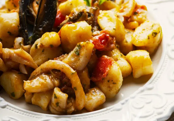 Gnocchi allo scoglio con cozze, calamari e pomodorini, un piatto ricco di sapori marini.