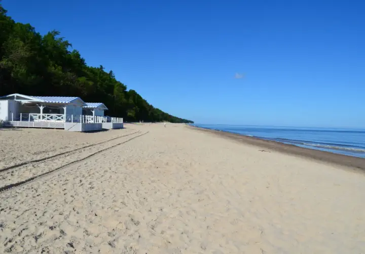 Pobierowo atrakcje: białe domki plażowe z niebieskimi markizami, piaszczysta plaża i spokojne morze pod błękitnym niebem.