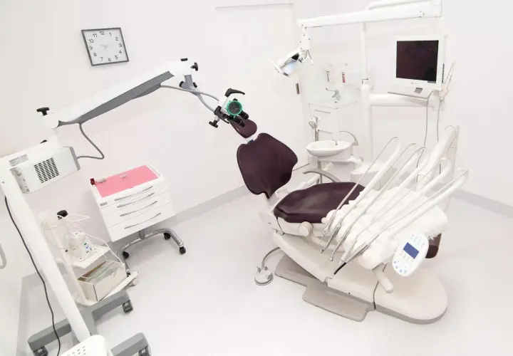 Nowoczesny gabinet stomatologiczny z fotelem, mikroskopem i sprzętem.