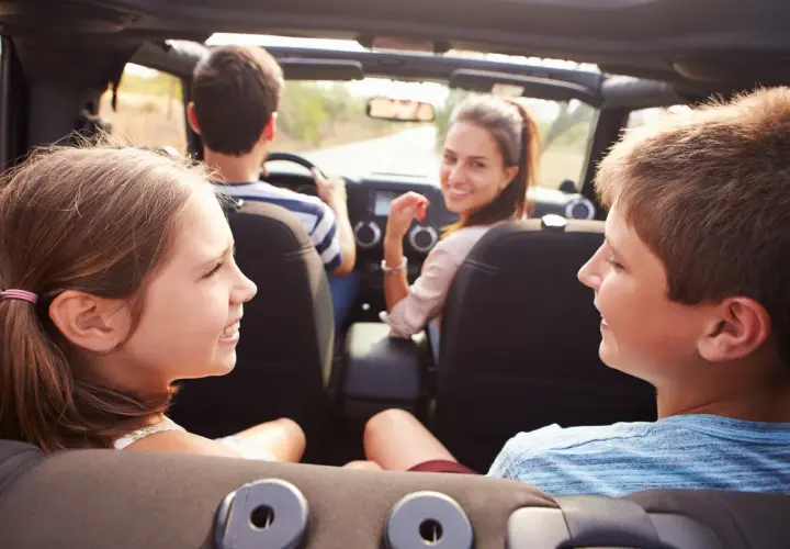 Famiglia in auto, divertiti con giochi da fare in macchina a voce. I bambini sorridono, la madre guarda indietro.