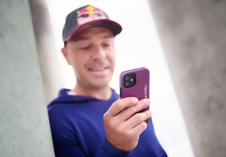 Mężczyzna w czapce Red Bull trzyma telefon z wzorzystym etui. Wzory na telefonie są czerwono-niebieskie.