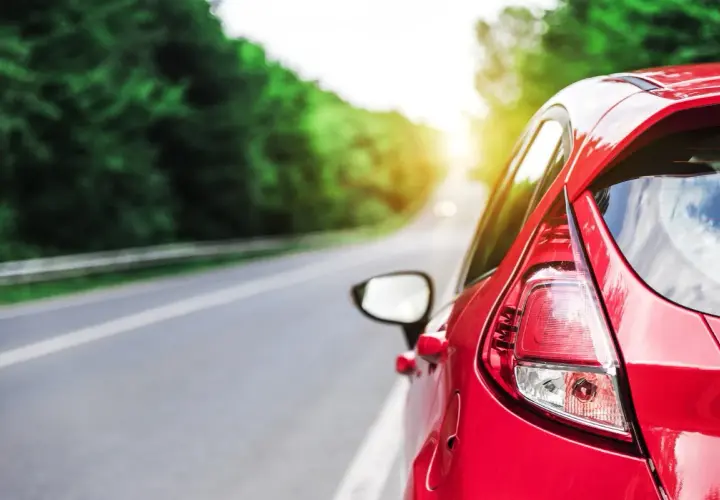 Auto rossa su strada panoramica, con sole che filtra tra gli alberi. Potrebbe indicare una **perdita potenza motore benzina** durante un viaggio.
