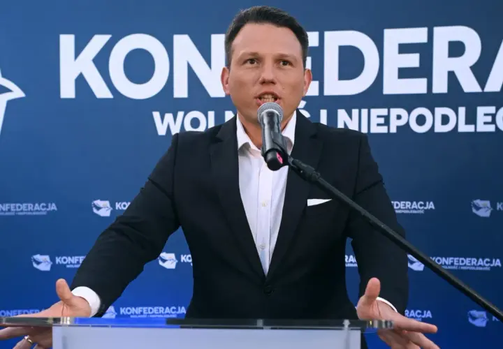 Mężczyzna w garniturze przemawia do mikrofonu na tle baneru Konfederacji. Dyskutuje, dlaczego KO chce odebrać dotacje partii opozycyjnej poprzez nowelizację kodeksu wyborczego.