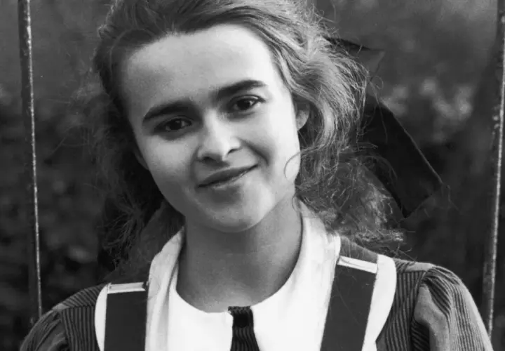 Młoda Helena Bonham Carter z burzą loków i figlarnym uśmiechem, w stroju przypominającym szkolny mundurek.