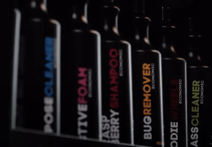 Rząd czarnych butelek z etykietami: "POSECLEANER", "CTIVEFOAM", "RASPBERRY SHAMPOO", "BUGREMOVER", "ODIE WHEELS", "ASSCLEANER". To są kosmetyki do samochodu.
