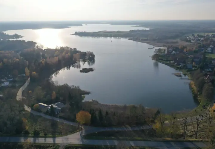 Jesioro Kałębie w jesiennej odsłonie, z widokiem na spokojną taflę wody, otoczoną drzewami w barwach złota i czerwieni.