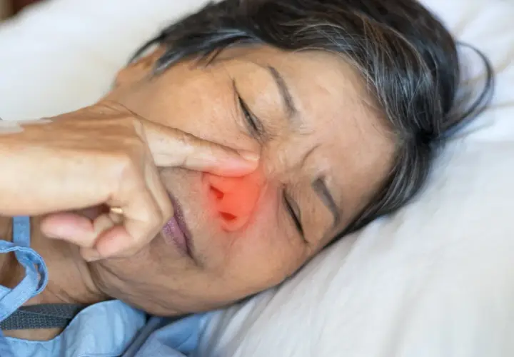 Una persona mayor con un dedo en la nariz, con una zona roja que indica dolor o irritación. ¿Qué pasa si te comes los mocos?