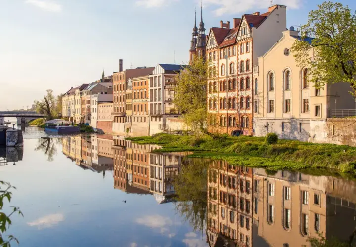 Nad rzeką w Opolu, zabytkowe kamienice odbijają się w spokojnej wodzie. To piękne opole atrakcje, które warto zobaczyć.