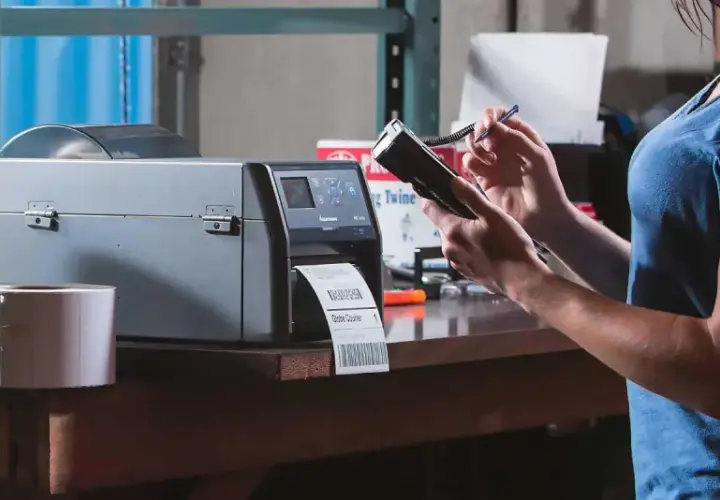 Frau bedient Drucker für Etiketten und Handscanner. Dies ermöglicht effizientes belegloses kommissionieren im Lager.