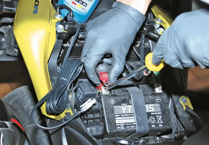 Mani guantate usano una chiave per staccare la batteria moto.