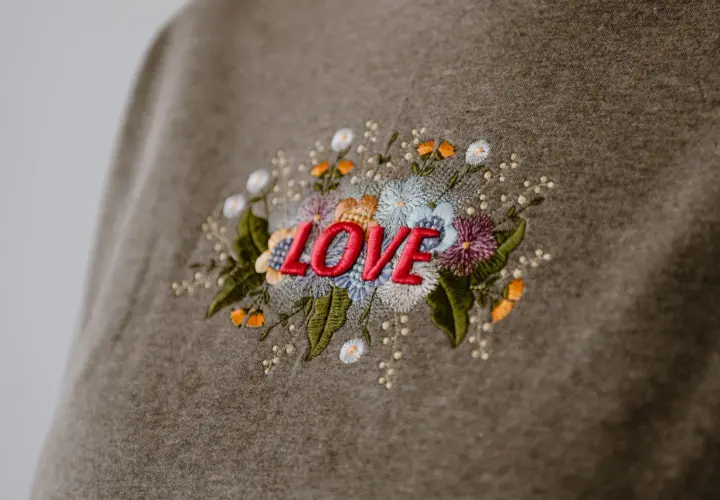 Besticktes Sweatshirt mit dem Wort "LOVE" umgeben von bunten Blumen. Zeigt, was man besticken kann.