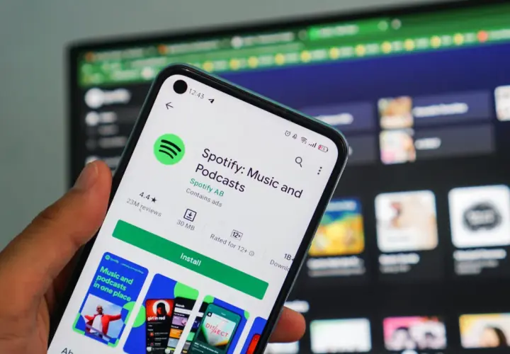Dłoń trzyma smartfon z ekranem sklepu Google Play, gdzie widoczna jest strona aplikacji Spotify. To świetna okazja, by skorzystać z **spotify promocja** i pobrać ulubioną muzykę i podcasty.