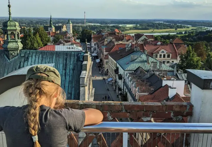 Widok z góry na Sandomierz, z dziewczynką w czapce na pierwszym planie. W oddali widać Wisłę i charakterystyczną Brama Opatowska.